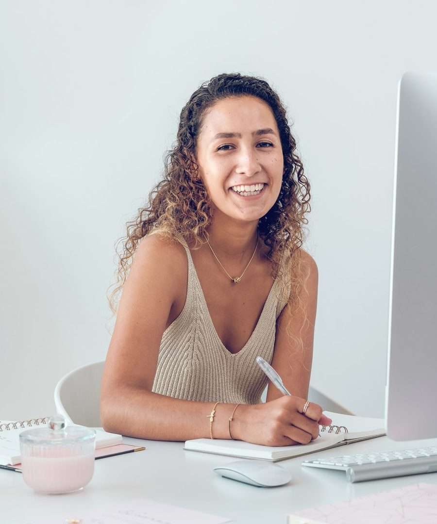 happy student sitting at table with computer and writing notes in planner e1656360940164