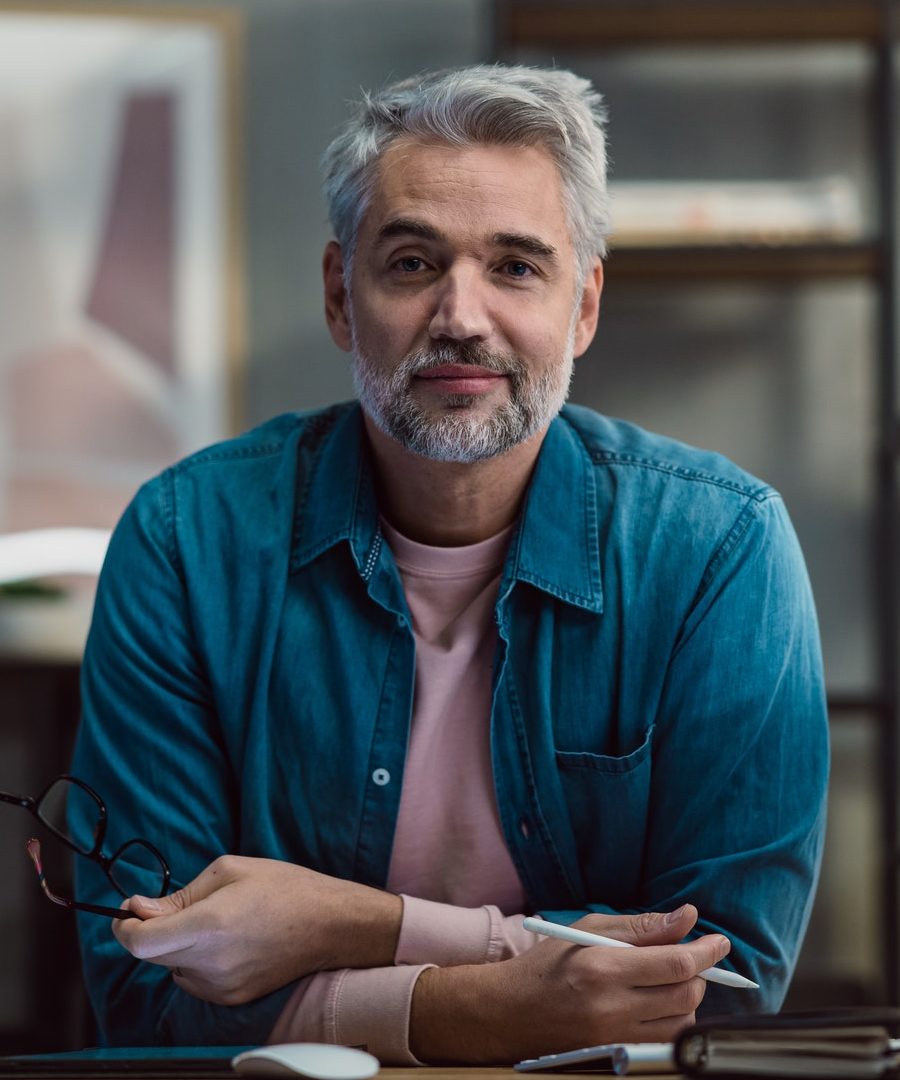 mature man architect working on tablet at desk indoors in office looking at camera e1656537506432