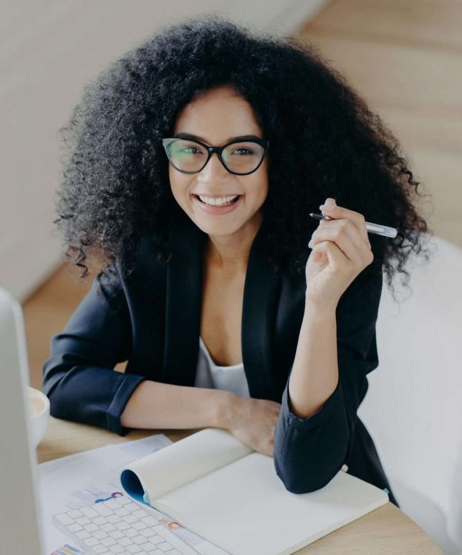 woman holds pen writes down some information works as editor looks gladfully e1656361925379